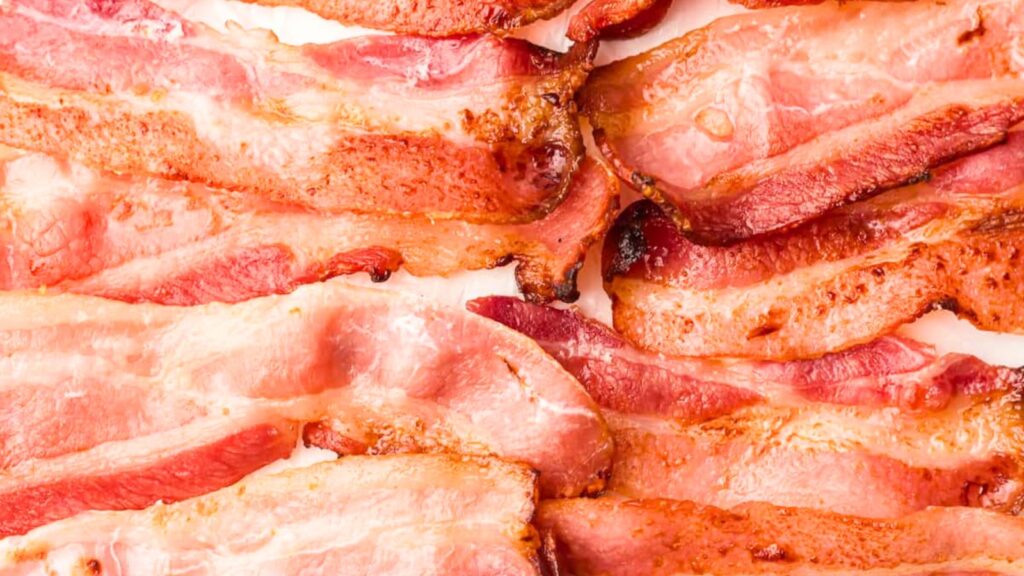 Several strips of cooked bacon are laid out close together on a flat surface.