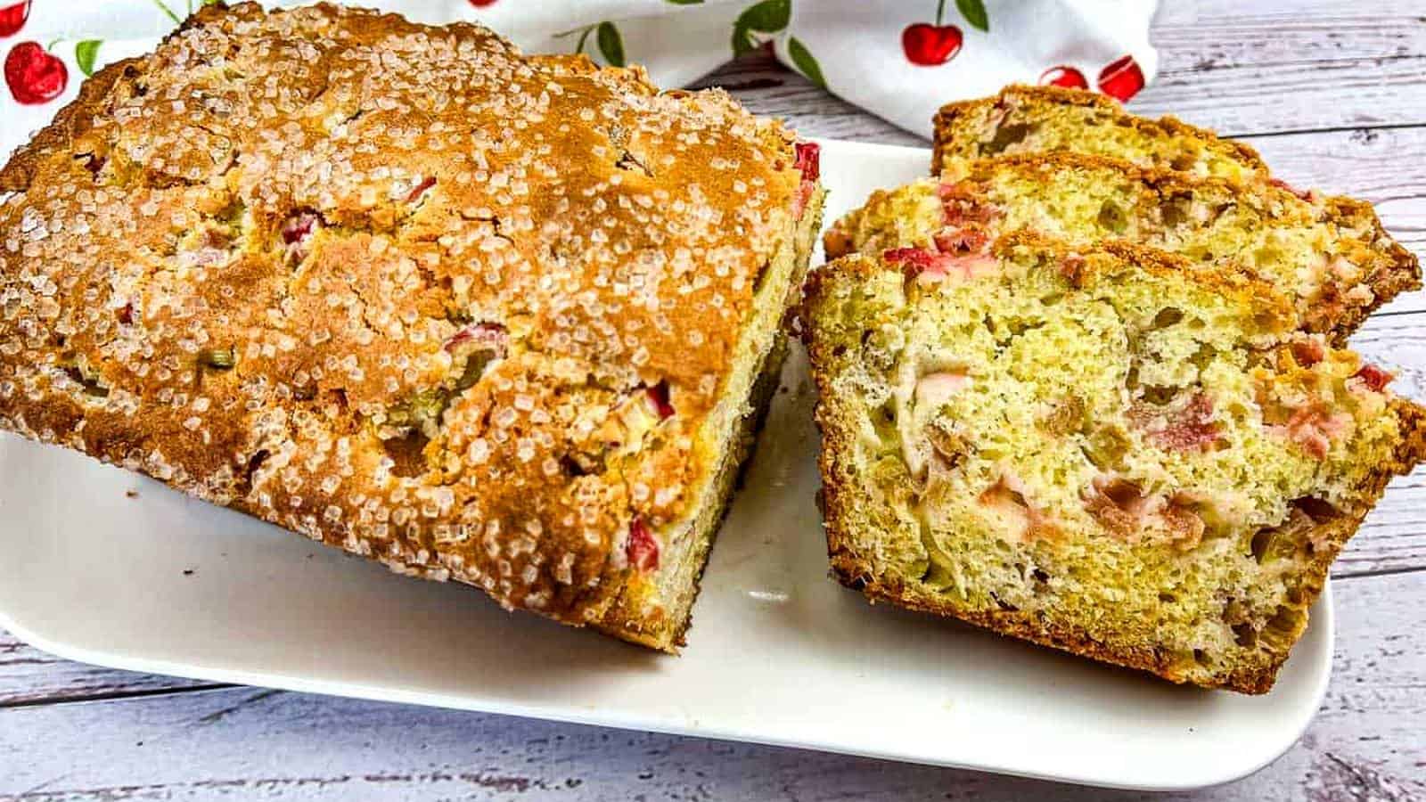 A loaf of Rhubarb Bread with a few slices on a white plate.