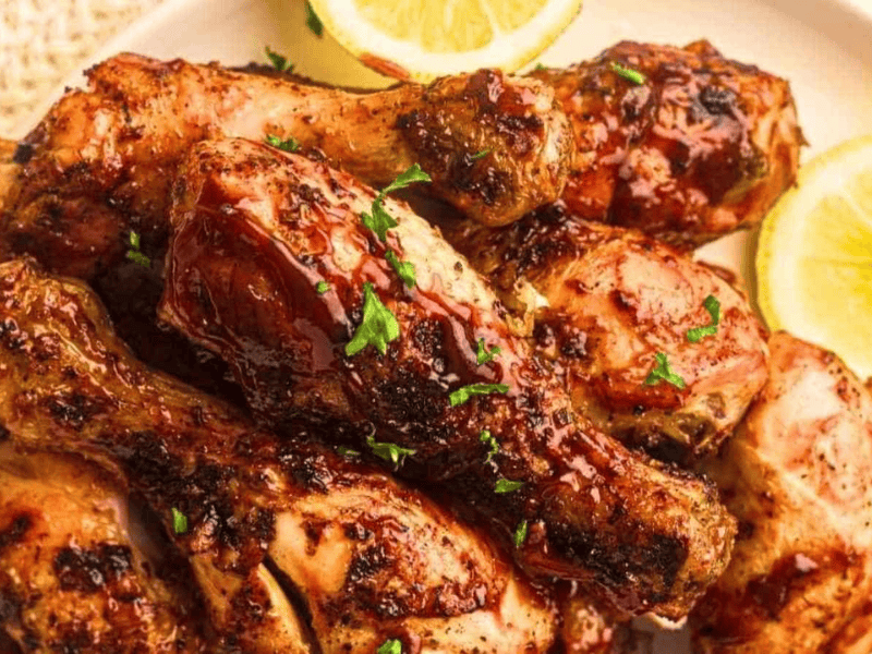 A plate of grilled chicken drumsticks garnished with chopped herbs, served with lemon slices.