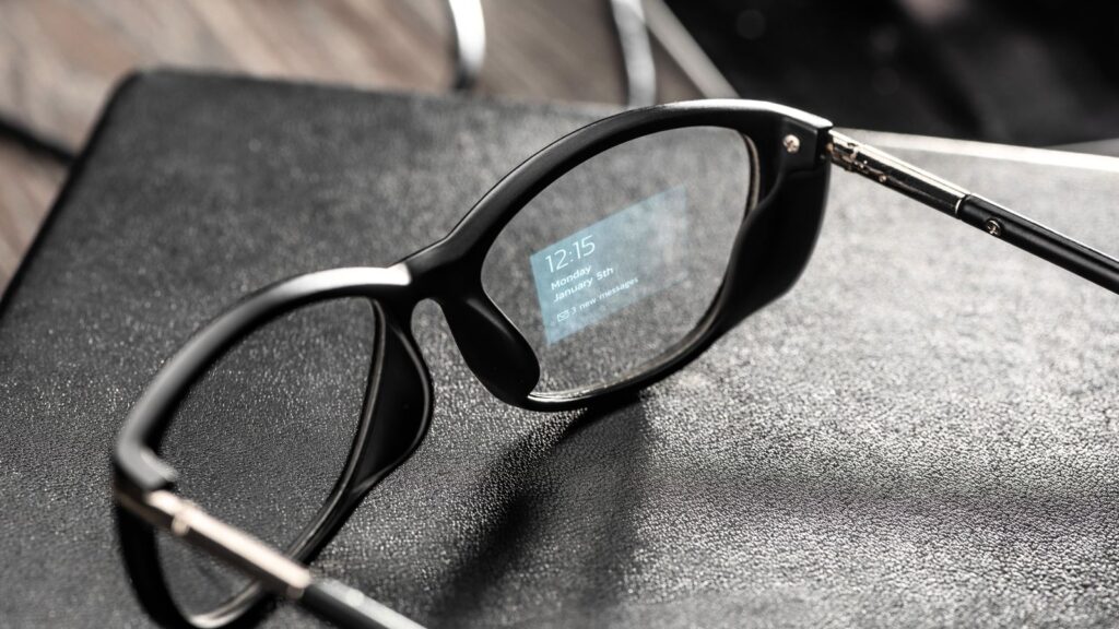 Black smart glasses rest on a textured surface, their sleek frame displaying the time and a notification on the inner right lens.
