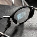 Black smart glasses rest on a textured surface, their sleek frame displaying the time and a notification on the inner right lens.