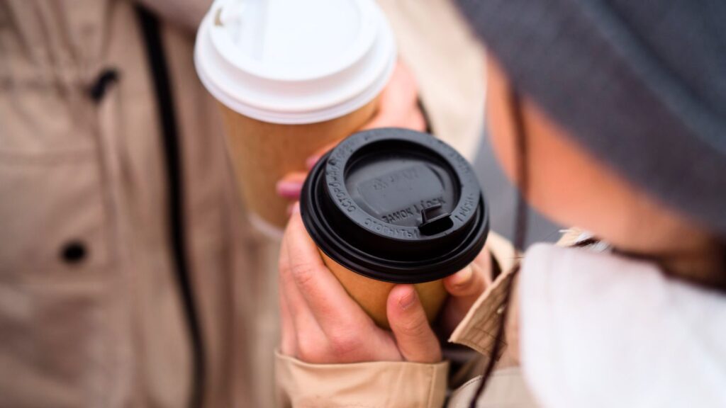 Two people holding disposable coffee cups with lids&mdash;perhaps reminiscent of grabbing Tom Hanks&rsquo; coffee at 7-Eleven&mdash;dressed in neutral outerwear, stand close together outdoors.