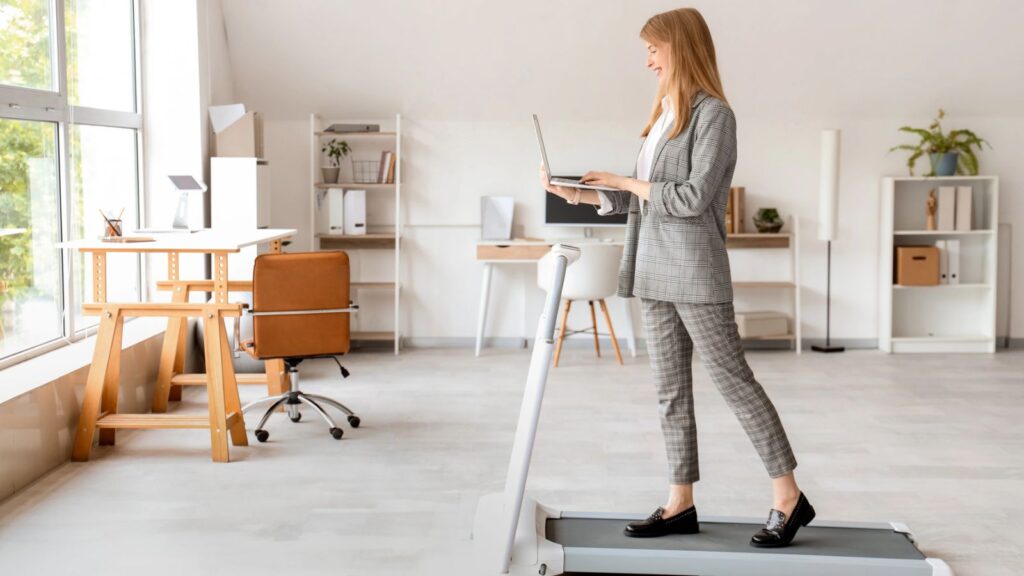 Woman in business attire works on a laptop while walking on a treadmill in a modern, bright office space, showcasing the versatility of walking pads for productive work environments.