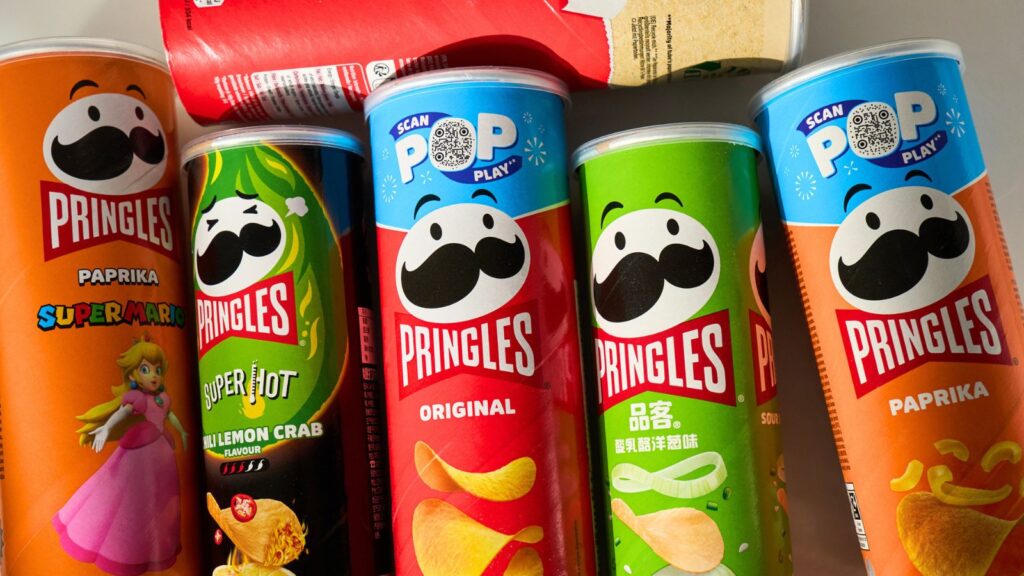 Six Pringles cans in various flavors and designs, including Super Mario and Pokemon Crab, are arranged side by side on a white surface.