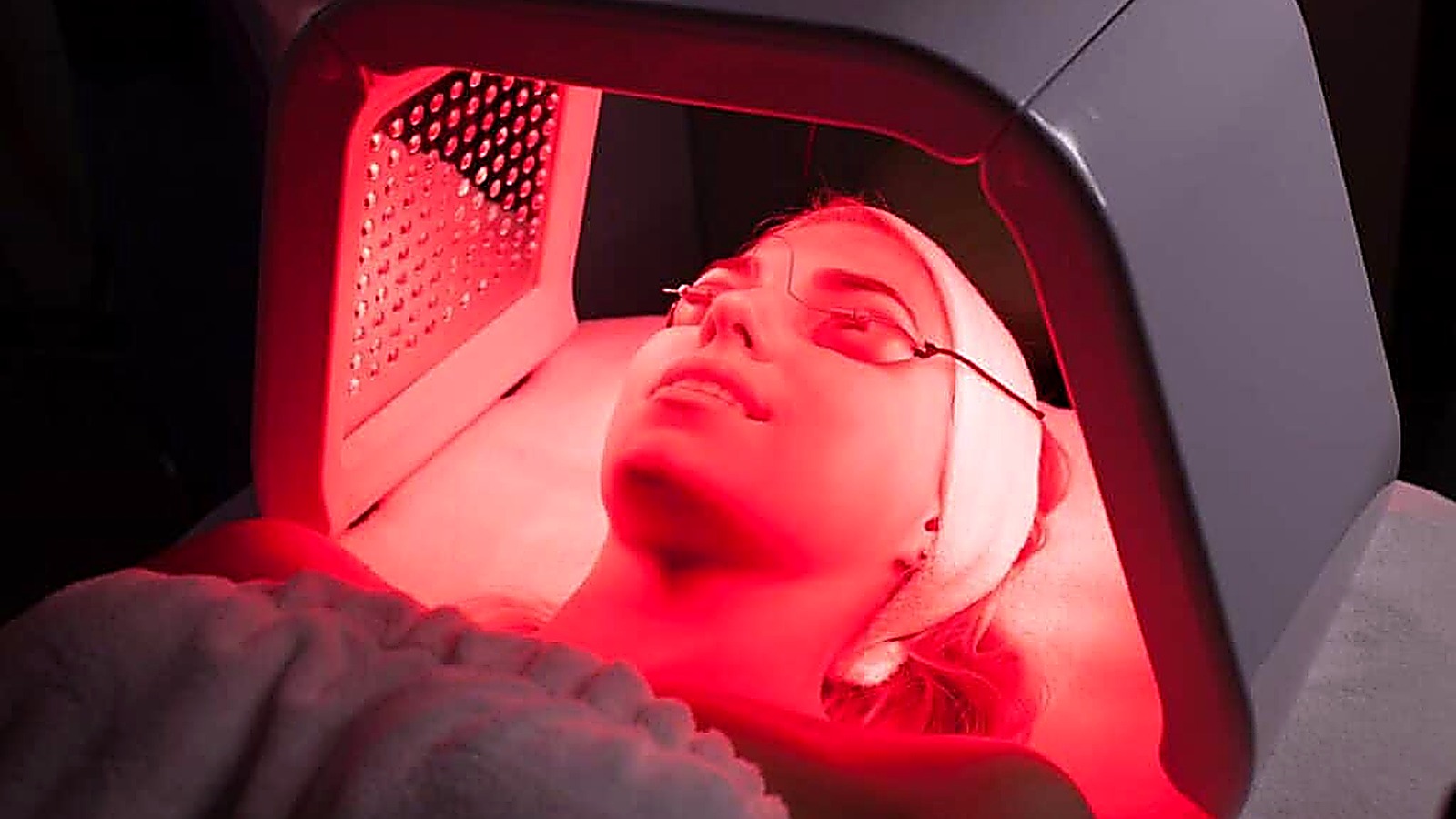 A person wearing protective goggles receives red light therapy on their face, lying under an LED light panel in a clinical setting, providing an insightful look into what is red light therapy and how it is administered.