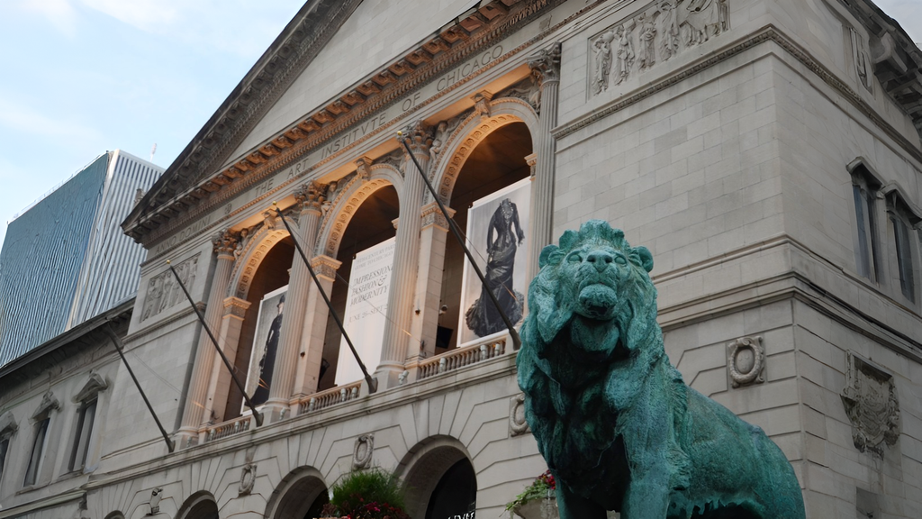 Front view of the Art Institute of Chicago, featuring its iconic bronze lion statue and banners hanging above the entrance.