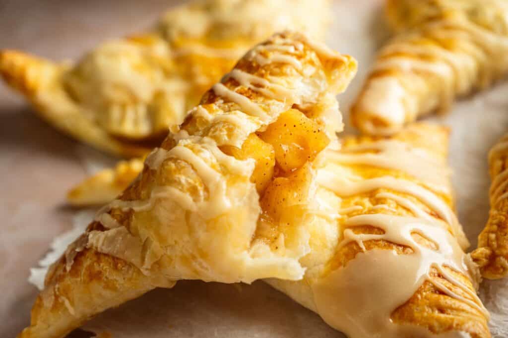 Close-up of glazed puff pastry turnovers filled with spiced apple filling, arranged on a light surface.