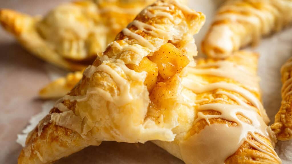 Close-up of flaky, golden-brown pastries filled with apple chunks and drizzled with white icing.