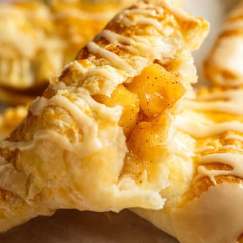Close-up of flaky, golden-brown pastries filled with apple chunks and drizzled with white icing.