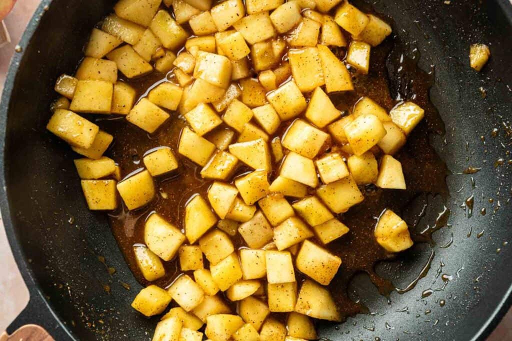 Diced apples cooked in a skillet with brown sugar and spices, creating a syrupy mixture.