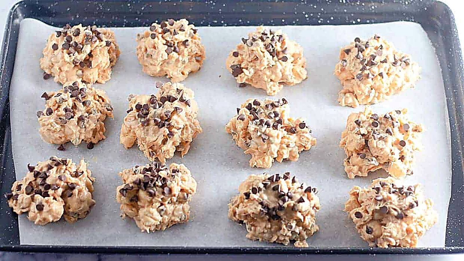 A baking tray lined with parchment paper holds twelve Avalanche Crunch Cookies.