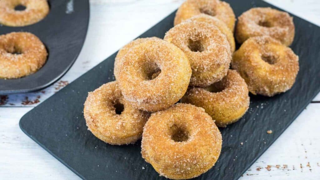 A black rectangular plate holds a stack of small, apple cider baked donuts.