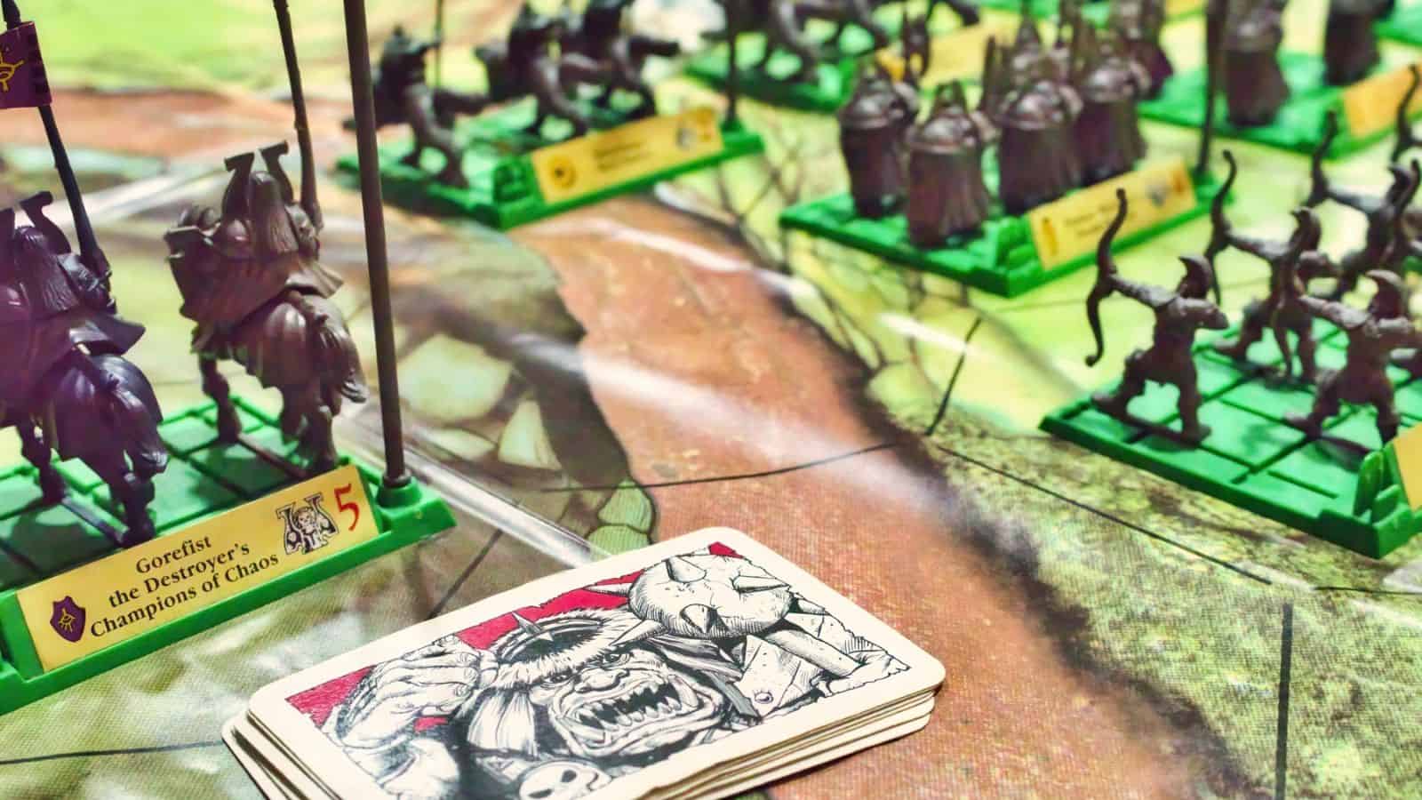Close-up of a tabletop fantasy board game featuring green plastic warrior figurines and a deck of illustrated cards on a colorful game map—perfect for fans of immersive board games.