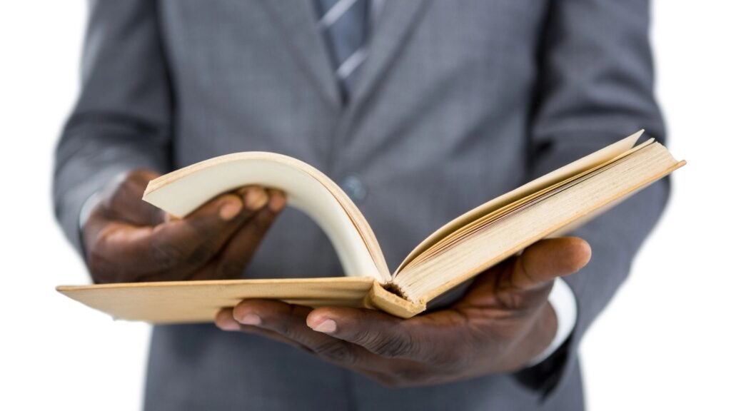 A person wearing a suit holds and flips through an open book with both hands against a white background, reminiscent of how you might remember if an encyclopedia salesman visited your home.