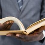 A person wearing a suit holds and flips through an open book with both hands against a white background, reminiscent of how you might remember if an encyclopedia salesman visited your home.