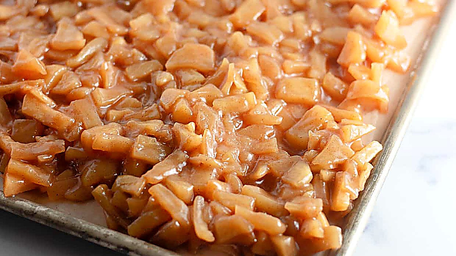 A baking tray filled with a layer of chopped apples coated in a cinnamon-sugar mixture.