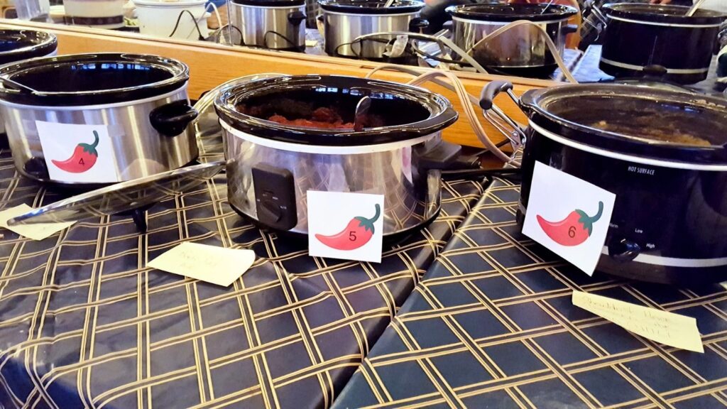 Three slow cookers labeled 4, 5, and 6 with chili pepper icons are lined up on a plaid tablecloth. Handwritten recipe cards are placed in front of each cooker.