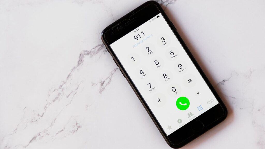 A smartphone on a white marble surface displays a dial pad with the number 911 entered, highlighting the importance of knowing emergency contacts for international travel.
