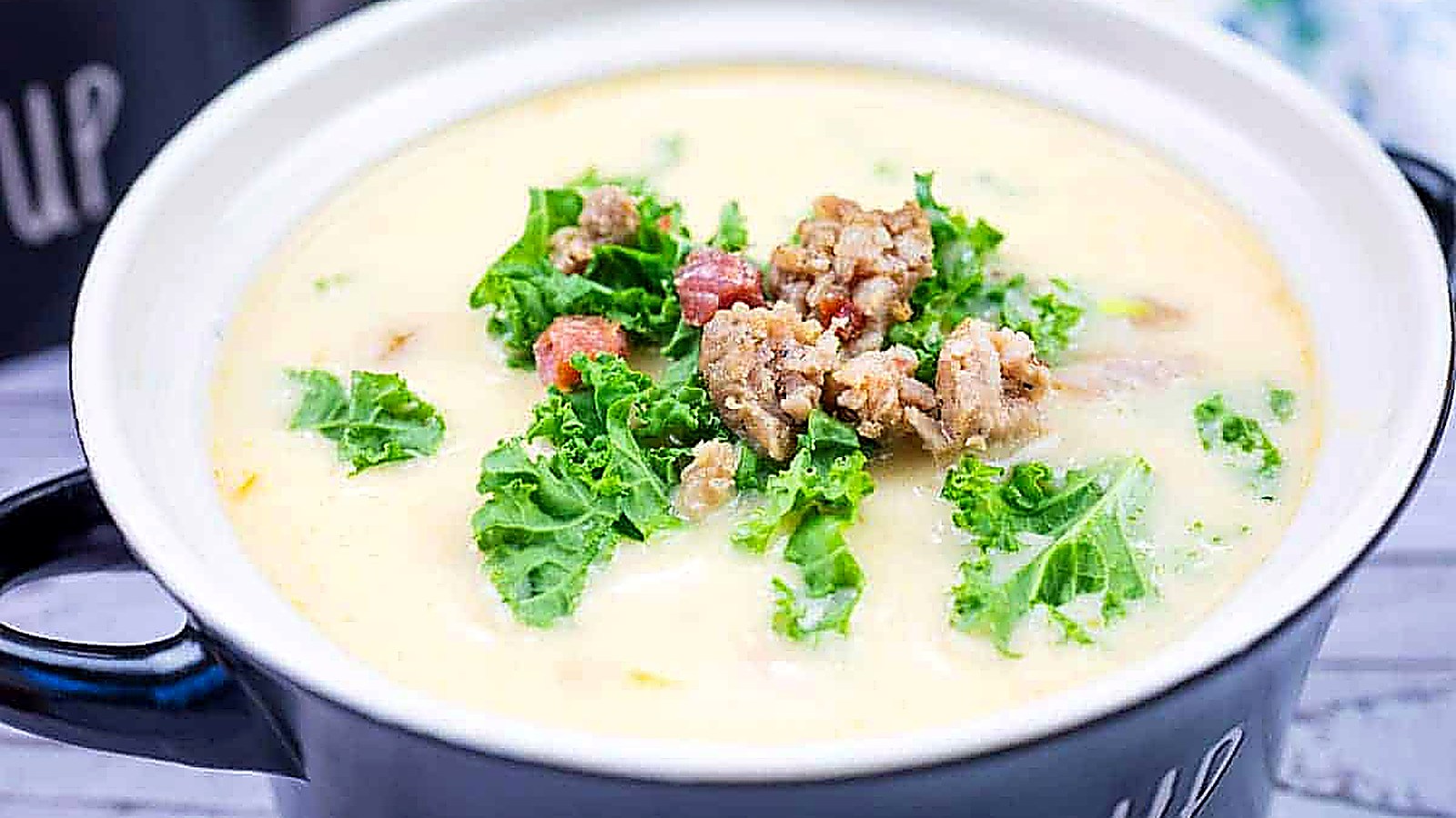 A bowl of Tuscan soup with sausage topped with kale and pancetta pieces in a black soup bowl.