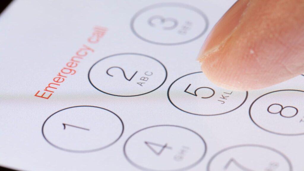 A close-up of a finger pressing the number 5 on a smartphone keypad screen with &ldquo;Emergency call&rdquo; written above the numbers, highlighting the importance of having emergency contacts for international travel readily accessible.