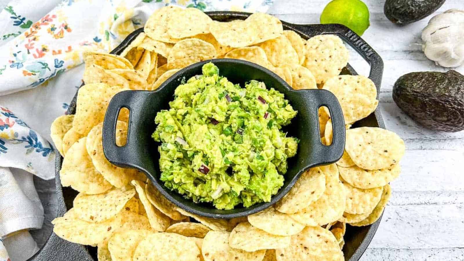 A small cast iron bowl of guacamole surrounded by tortilla chips in a larger skillet.