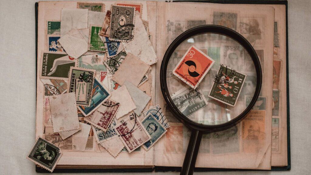 Open stamp album with assorted stamps scattered on the pages, and a magnifying glass focusing on a red stamp, reminiscent of trading S&H Green Stamps from years past.