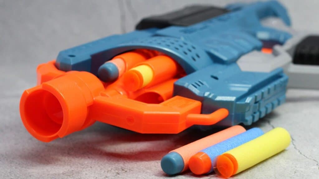 Close-up of a blue and orange toy dart gun with foam darts in the chamber and more foam darts lying beside it on a gray surface&mdash;one of the latest toy fads that&rsquo;s sure to be at the top of every kid&rsquo;s wish list.