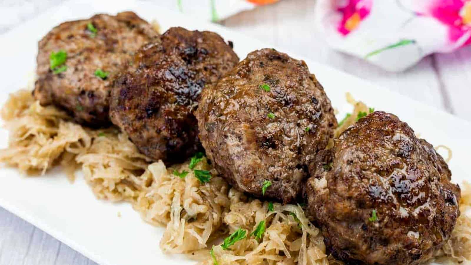 Four browned meat patties are served on a bed of shredded cooked cabbage on a white rectangular plate.