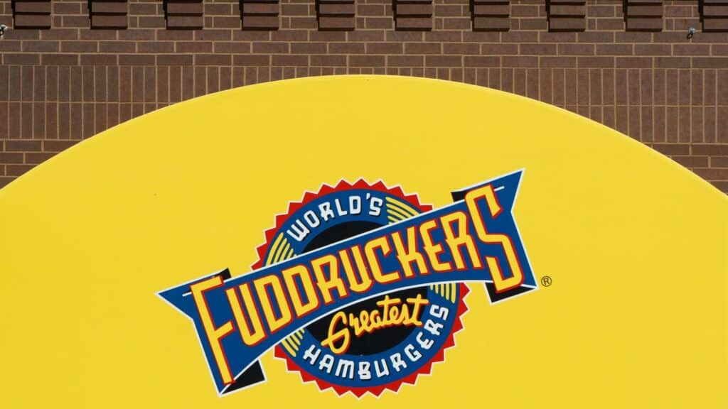 Fuddruckers sign with the text &ldquo;World&rsquo;s Greatest Hamburgers&rdquo; on a yellow background, mounted on a brick wall&mdash;a proud symbol among restaurant chains that came back.