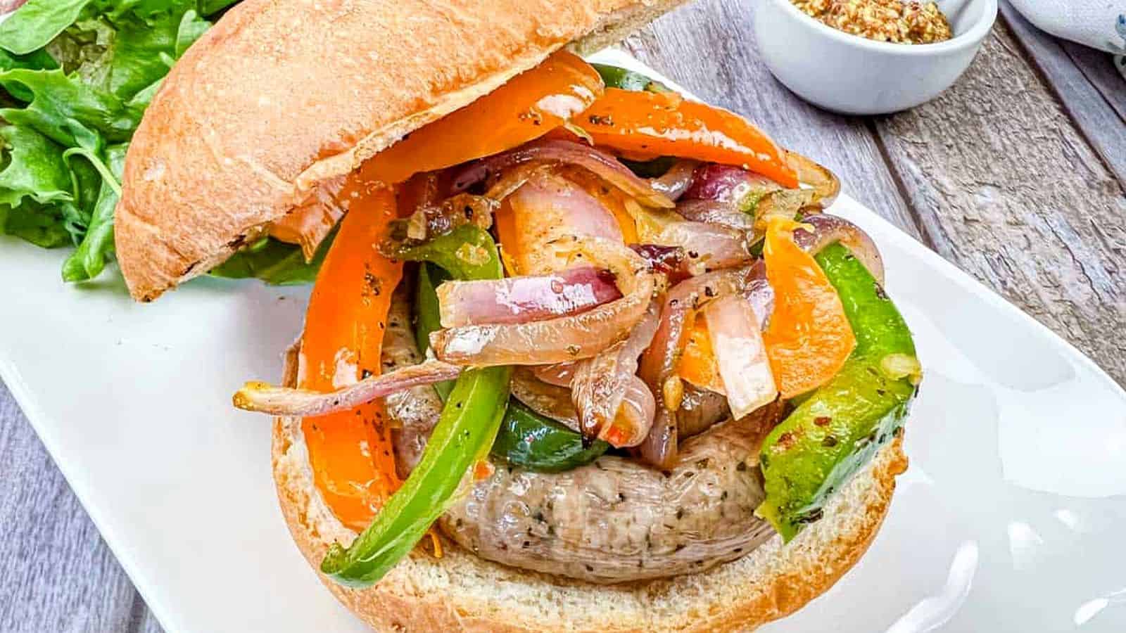 A sandwich with grilled sausage & peppers, and onions on a plate.