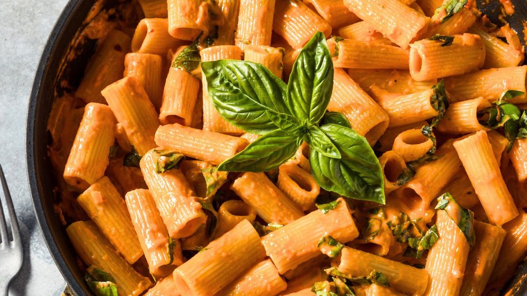 Spicy rigatoni vodka pasta with creamy tomato sauce, garnished with fresh basil leaves, served in a black pan.