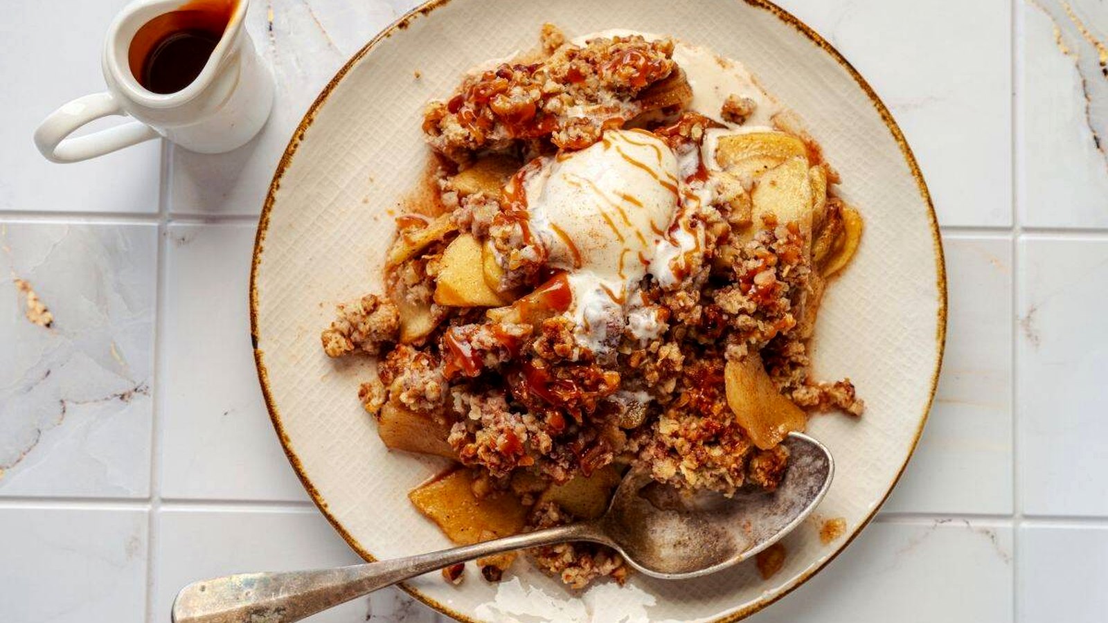 A plate of Classic Apple Crisp with a scoop of vanilla ice cream, served with a spoon.