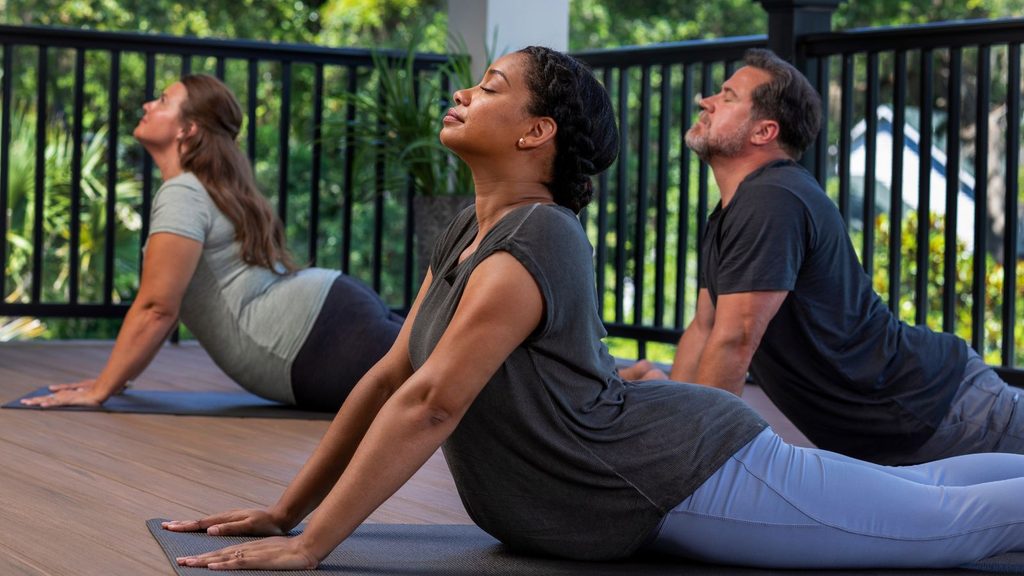 Three people practice yoga outdoors on mats, performing the upward-facing dog pose on a wooden deck with greenery in the background, embracing mindful movement and glp-1 support for overall well-being.