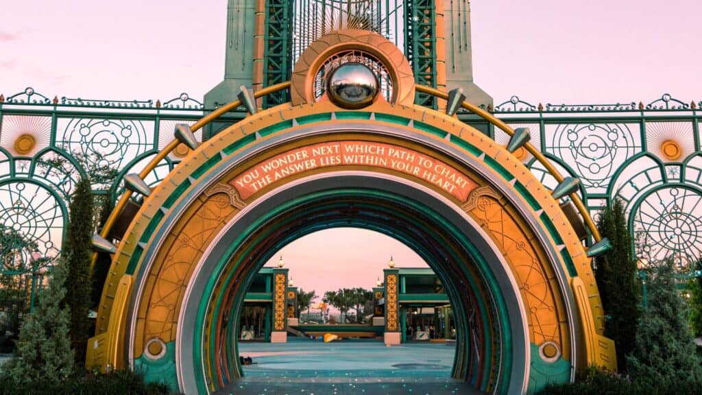 An ornate archway with a sign reading, &ldquo;You wonder which path to chart; the answer lies within your heart,&rdquo; set against a colorful and decorative structure with greenery nearby, subtly invites visitors to embark on their own adventure&mdash;while reminding all to respect Disney and Universal theme park rules along the way.