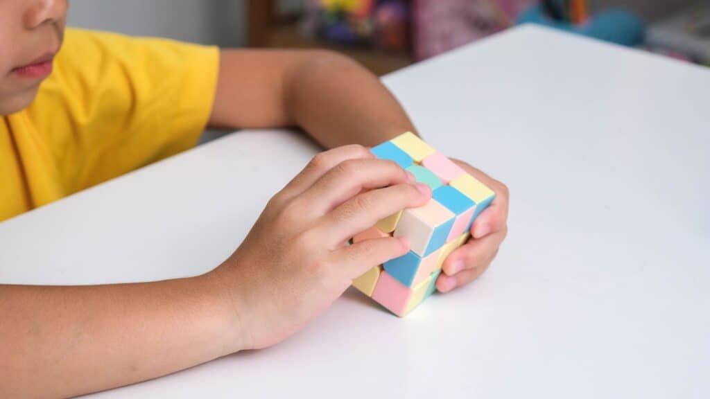 A child wearing a yellow shirt is sitting at a white table, solving a pastel-colored Rubik&rsquo;s Cube&mdash;one of this year&rsquo;s top toy fads and sure to be on every kid&rsquo;s wish list.