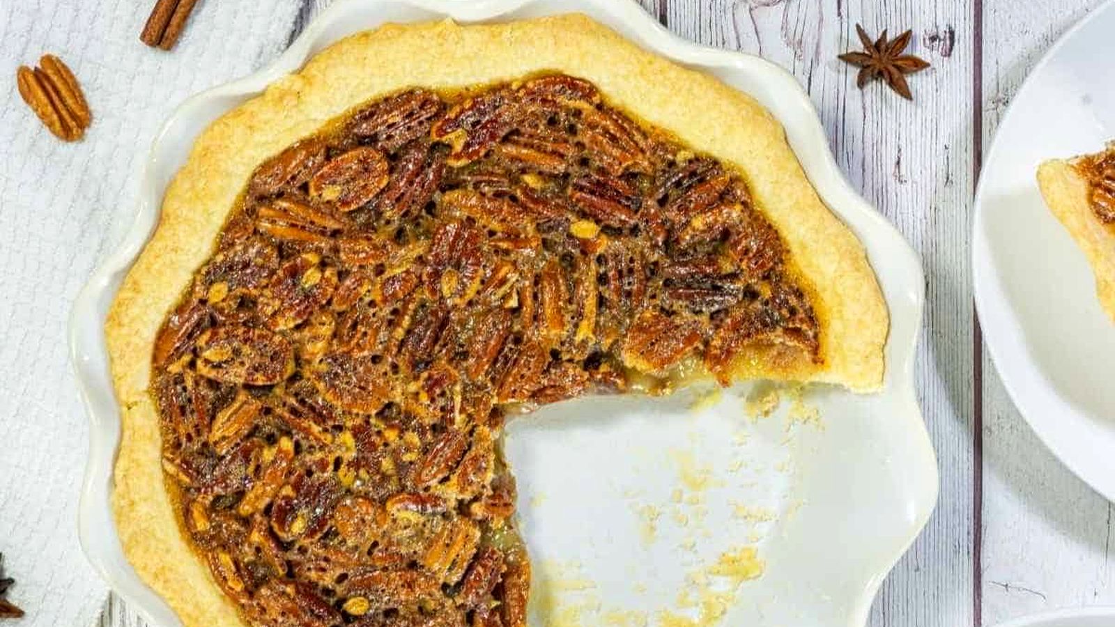 A pecan pie in a white dish with a large slice missing, shown on a light wooden surface.