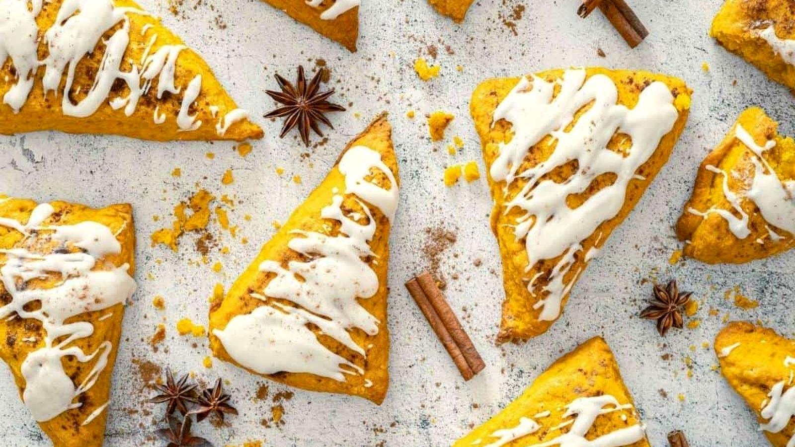 Pumpkin Spice Scones with Vanilla Glaze are arranged on a light surface, surrounded by cinnamon sticks and star anise.