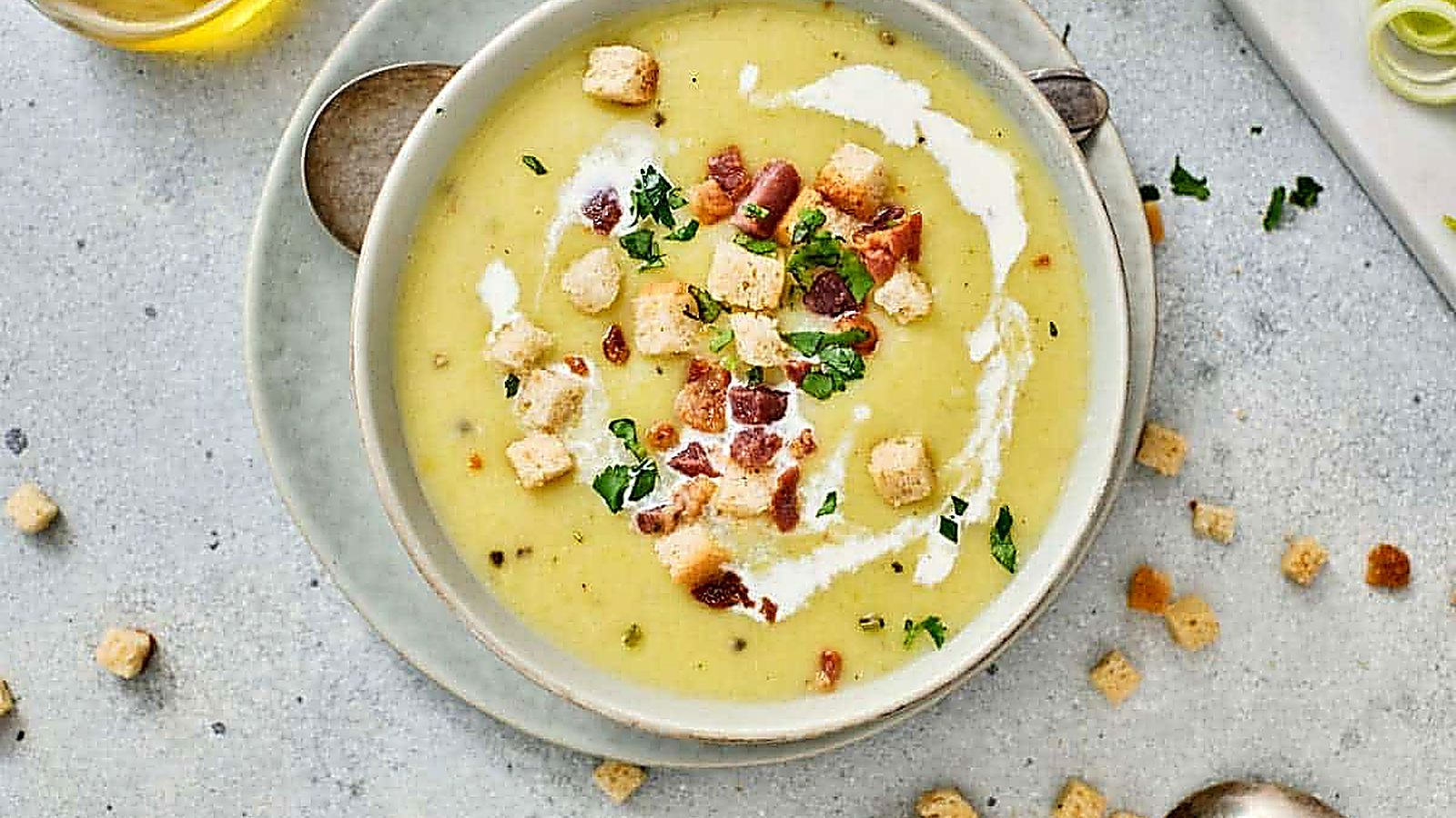 A bowl of Gordon Ramsay's Leek & Potato Soup is placed on a plate with a spoon nearby.