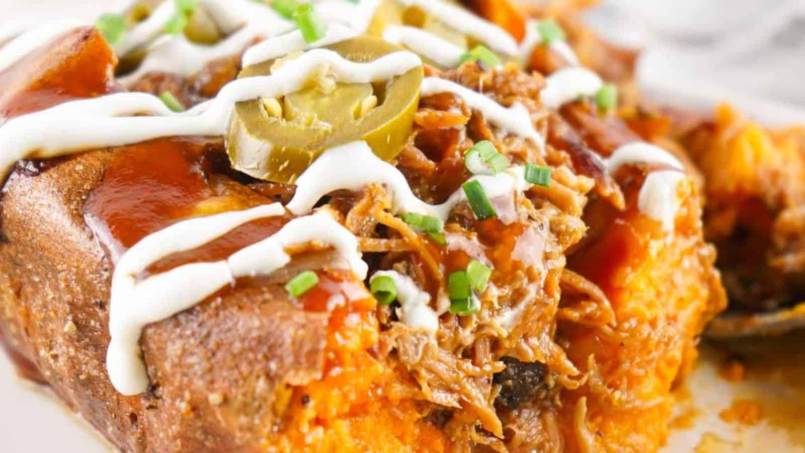 Close-up of a loaded pulled pork baked potato topped with shredded meat, barbecue sauce, sliced jalapeños, chopped chives, and drizzled with sour cream.