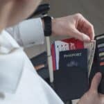 A person holding a travel wallet containing a passport, airline boarding pass, and U.S. currency to ensure they are prepared in case a debit card is declined abroad.