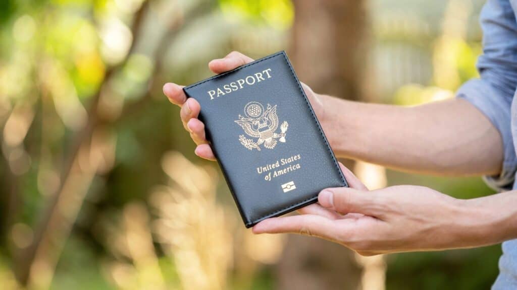 A person holds a closed United States passport with both hands outdoors, with a blurred green background, perhaps ready to explore on one of the national park fee free days.