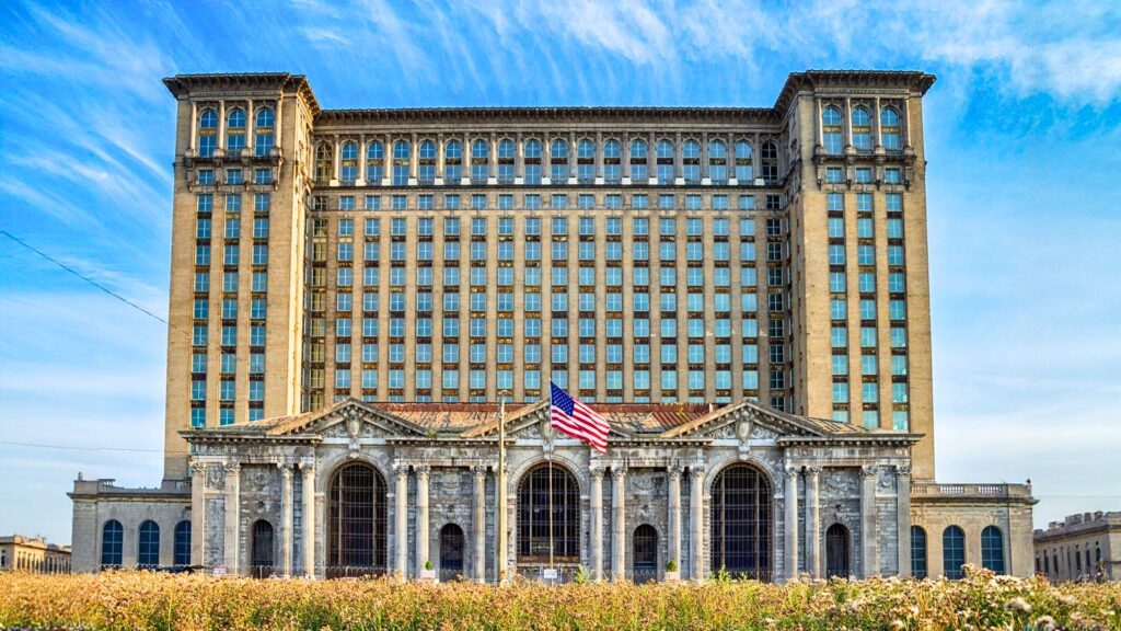Large, historic building with arched windows and columns, an American flag in front, and a blue sky overhead.