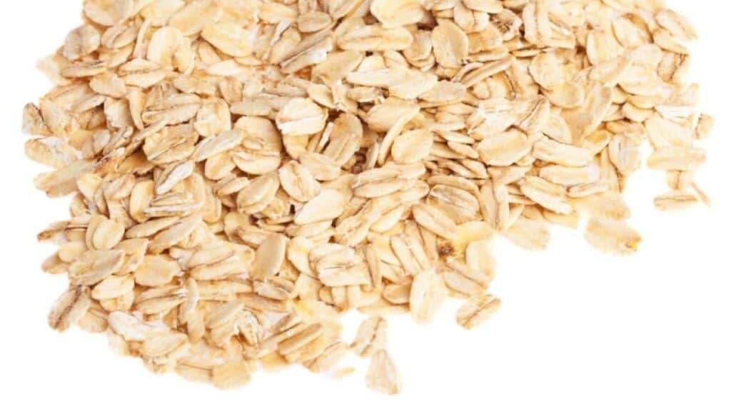 A pile of uncooked rolled oats from food brands companies you know is scattered on a white background.