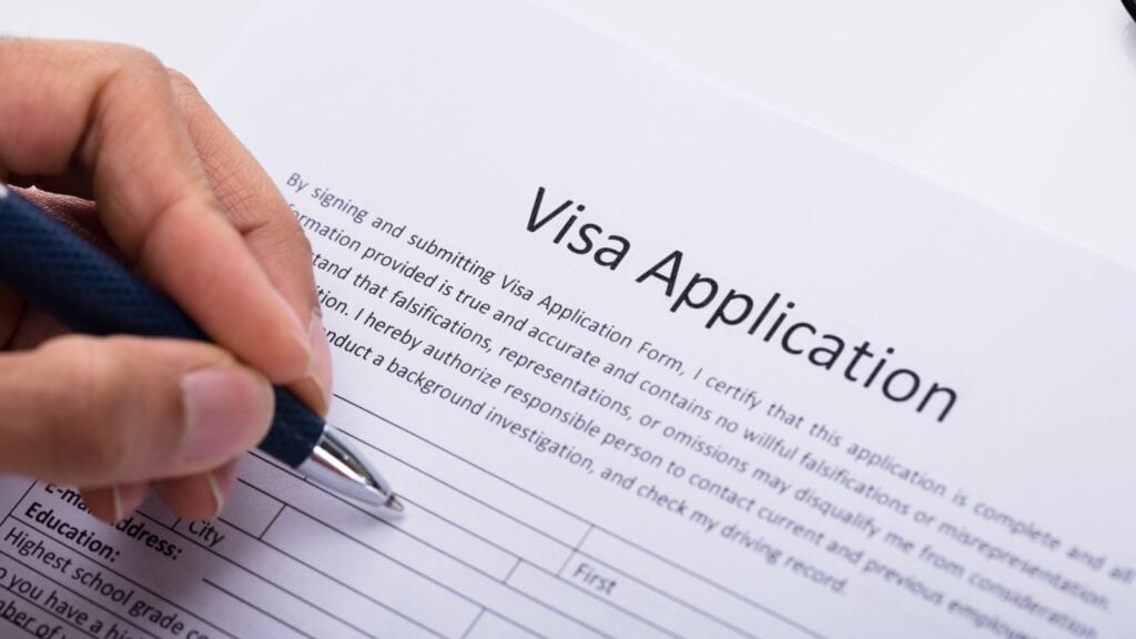 A person holds a pen and fills out a visa application form on a desk, as US tourists need approval first before traveling.