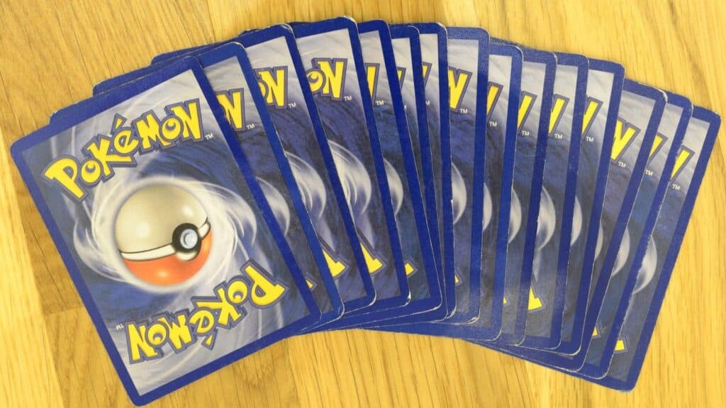 A fan of Pok&eacute;mon trading cards is showing several cards face down, spread out in a fan shape on a wooden surface&mdash;a nostalgic nod to playground fads that ruled recess.