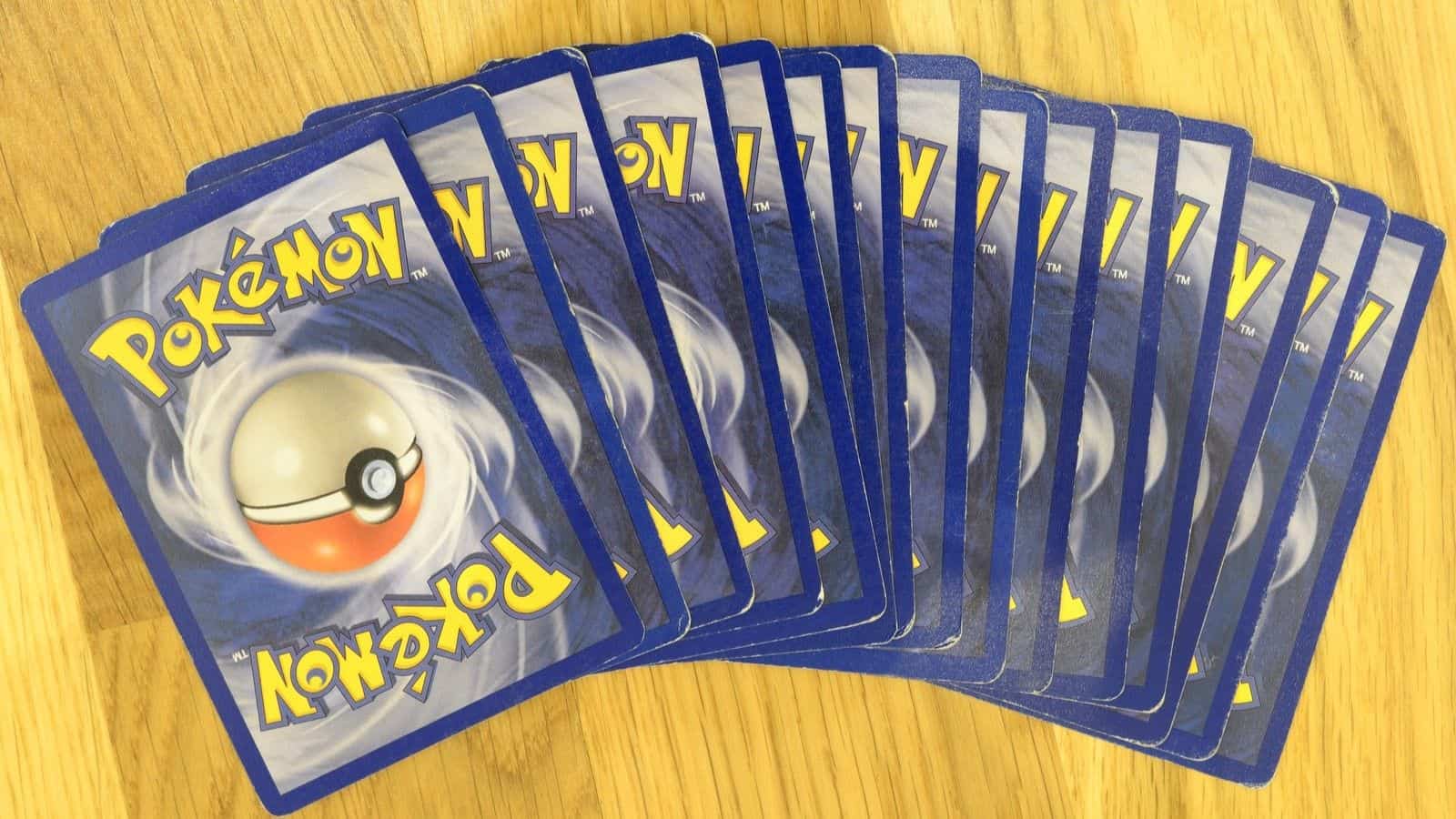 A fan of Pokémon trading cards is showing several cards face down, spread out in a fan shape on a wooden surface—a nostalgic nod to playground fads that ruled recess.