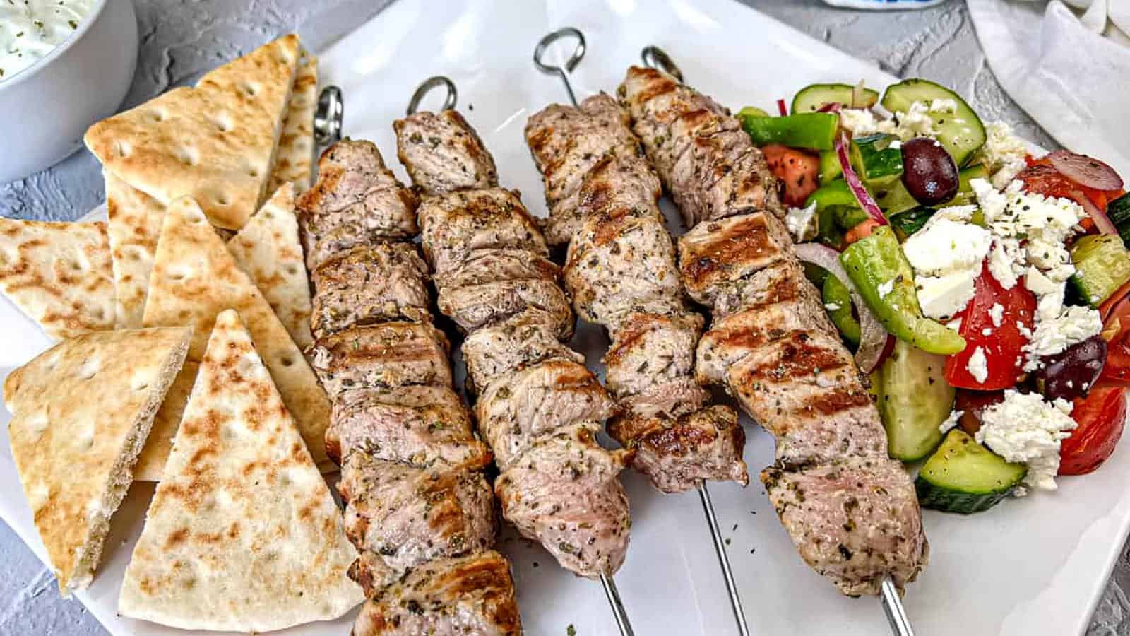 Ninja Woodfire Pork Souvlaki with Horiatiki Salad and pita bread on a white plate.