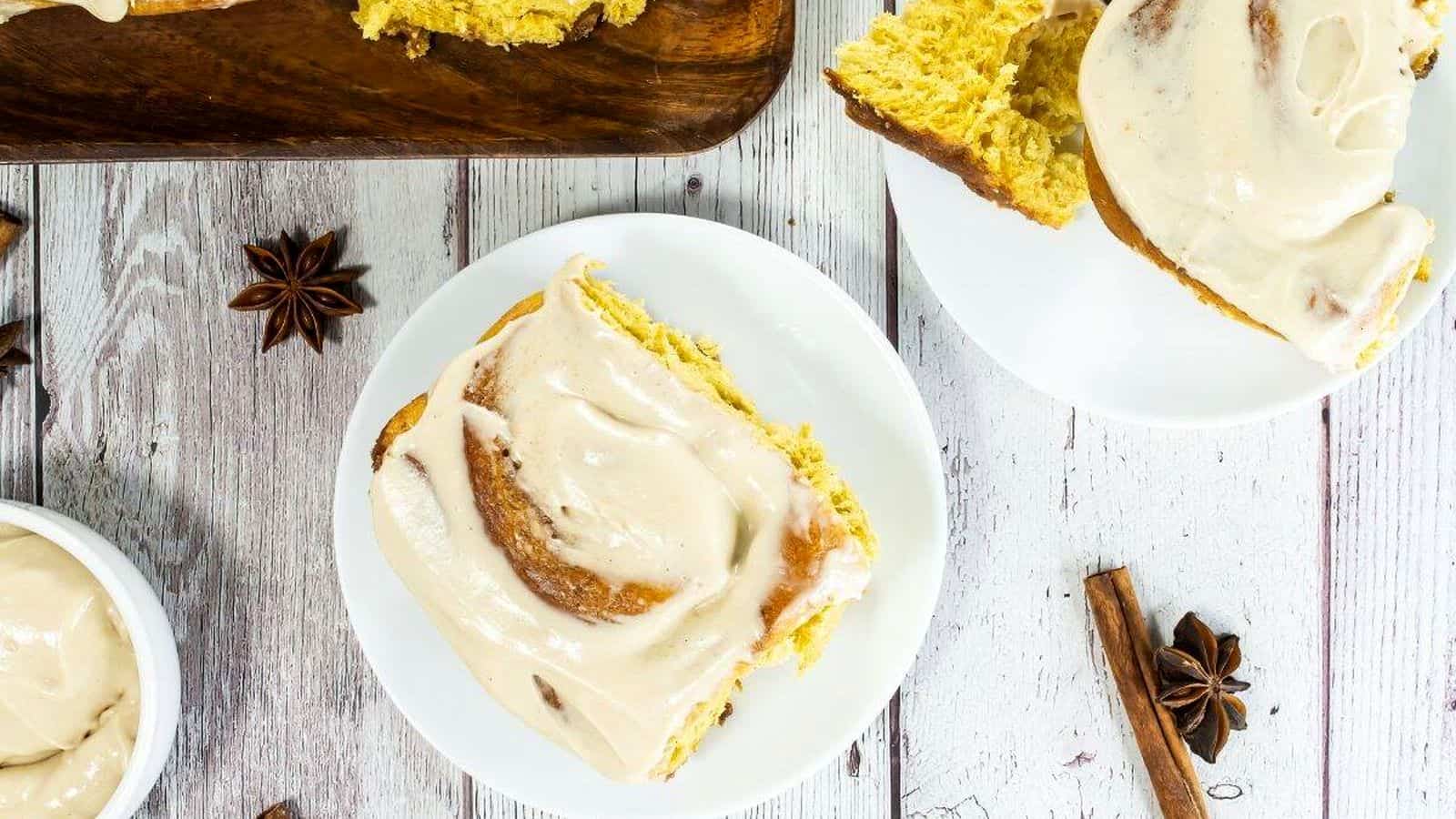 Homemade cinnamon rolls with cream cheese frosting on wooden serving board.