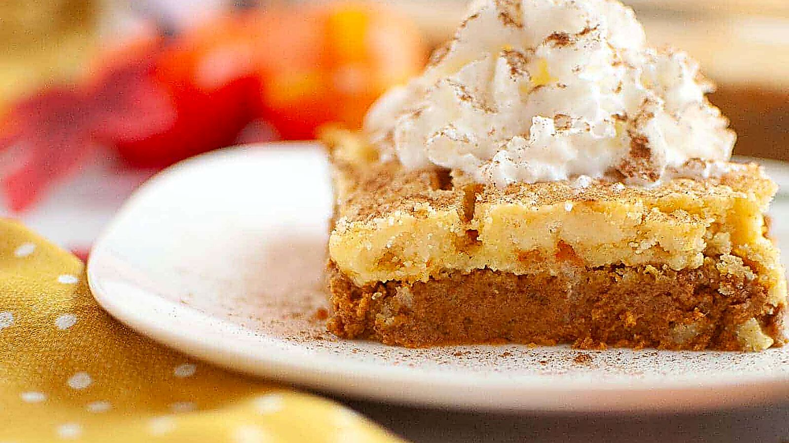 A slice of layered pumpkin dessert topped with whipped cream and a sprinkle of cinnamon on a white plate.