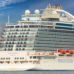 A large white cruise ship labeled “Regal Princess” is docked near a city waterfront with tall buildings in the background.
